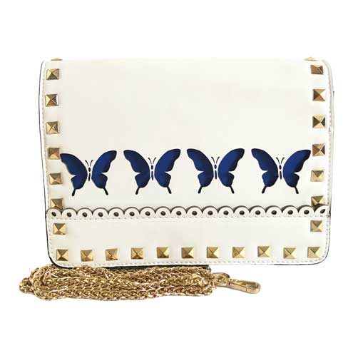 Mensajera para dama HNA de color blanco con estampado de 4 mariposas en color azul en la parte de enfrente del producto, asa en material metálico de color dorado, detalles decorativos metálicos en color dorado.
