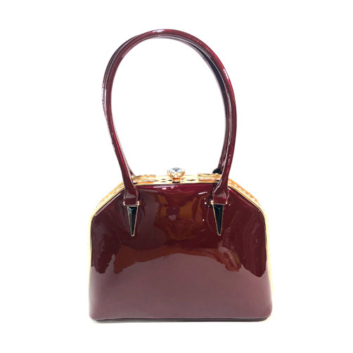 Bolsa Verchelli de color Rojo granate, material charol, en sus partes extremas viene en el mismo color, broche en la parte superior para cerrar la bolsa en material metálico y de color dorado, asa estática de color rojo granate para llevar a la mano, detalles metálicos en color dorado con incrustaciones de diamantes decorativos en la parte superior de la bolsa y broche.